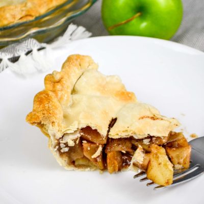 classic brandy apple pie slice on white plate with granny smith apple